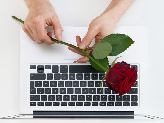 Eine Frau hält eine Rose über einer Laptop-Tastatur. 
