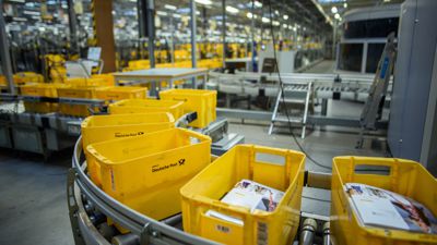 Gelbe Kisten zum Sortieren von Briefen laufen im Briefzentrum Kiel der Deutschen Post über ein Förderband. 