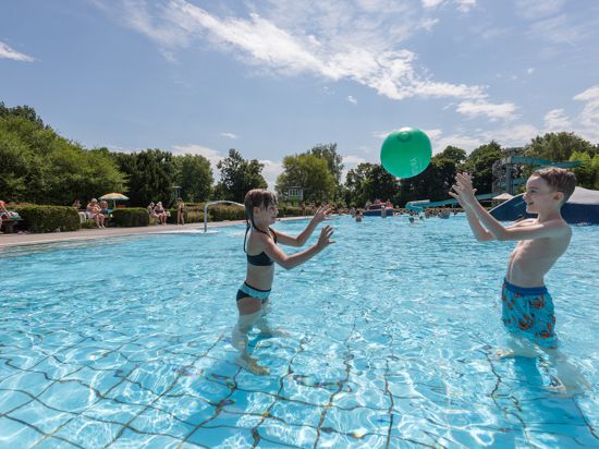 Ein Mädchen und ein Junge spielen Ball in einem Schwimmbad. 