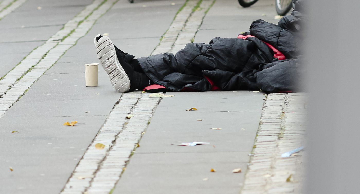 Ein Mann sitzt in einen Schlafsack gehüllt auf dem Asphalt in der Innenstadt.