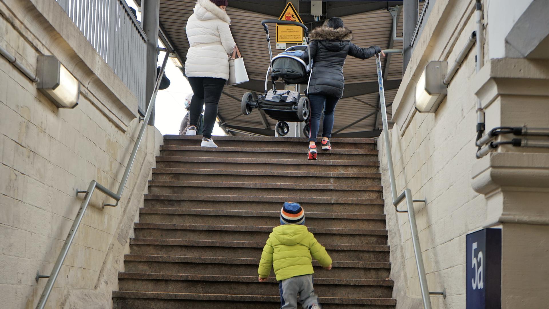 Eine Frau trägt einen Kinderwagen eine Treppe hoch.