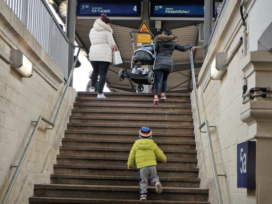 Eine Frau trägt einen Kinderwagen eine Treppe hoch.