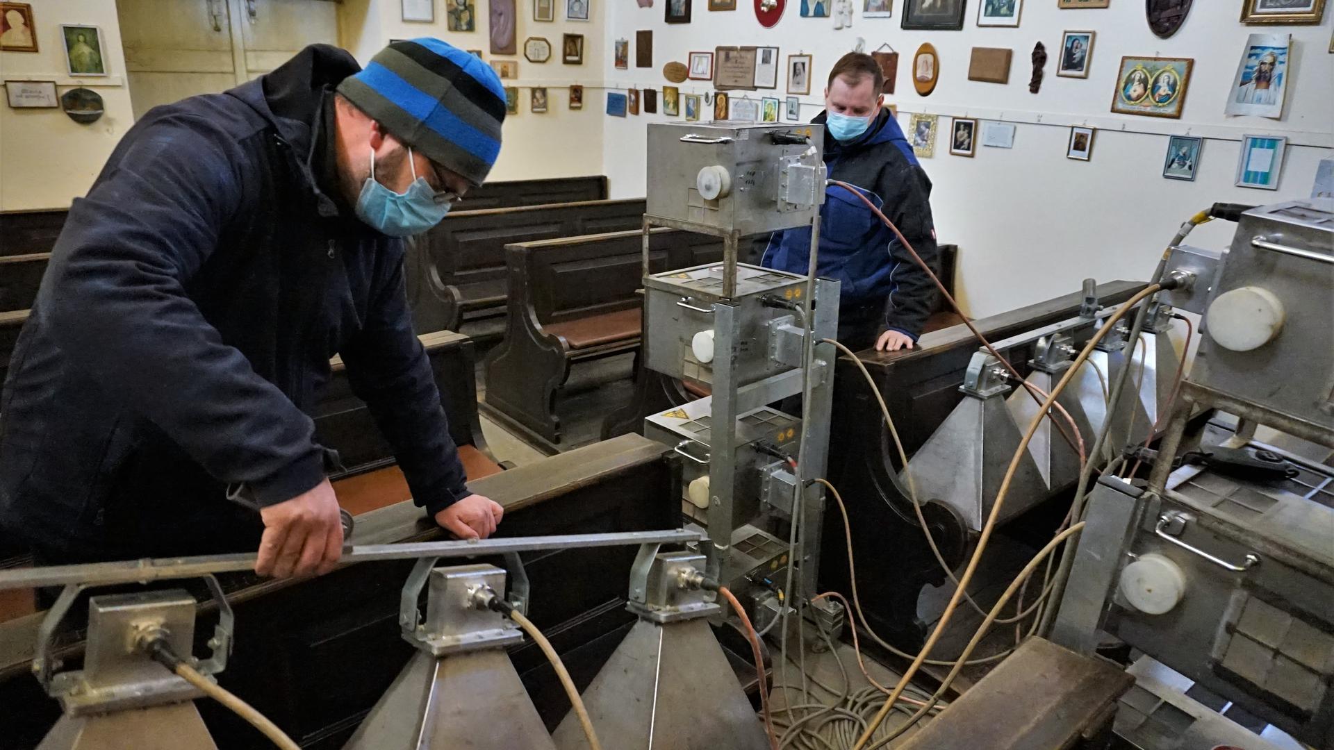 Zwei Männer bestrahlen hölzerne Kirchenbänke mit Mikrowellen-Geräten gegen Holzwürmer