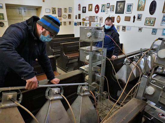 Zwei Männer bestrahlen hölzerne Kirchenbänke mit Mikrowellen-Geräten gegen Holzwürmer