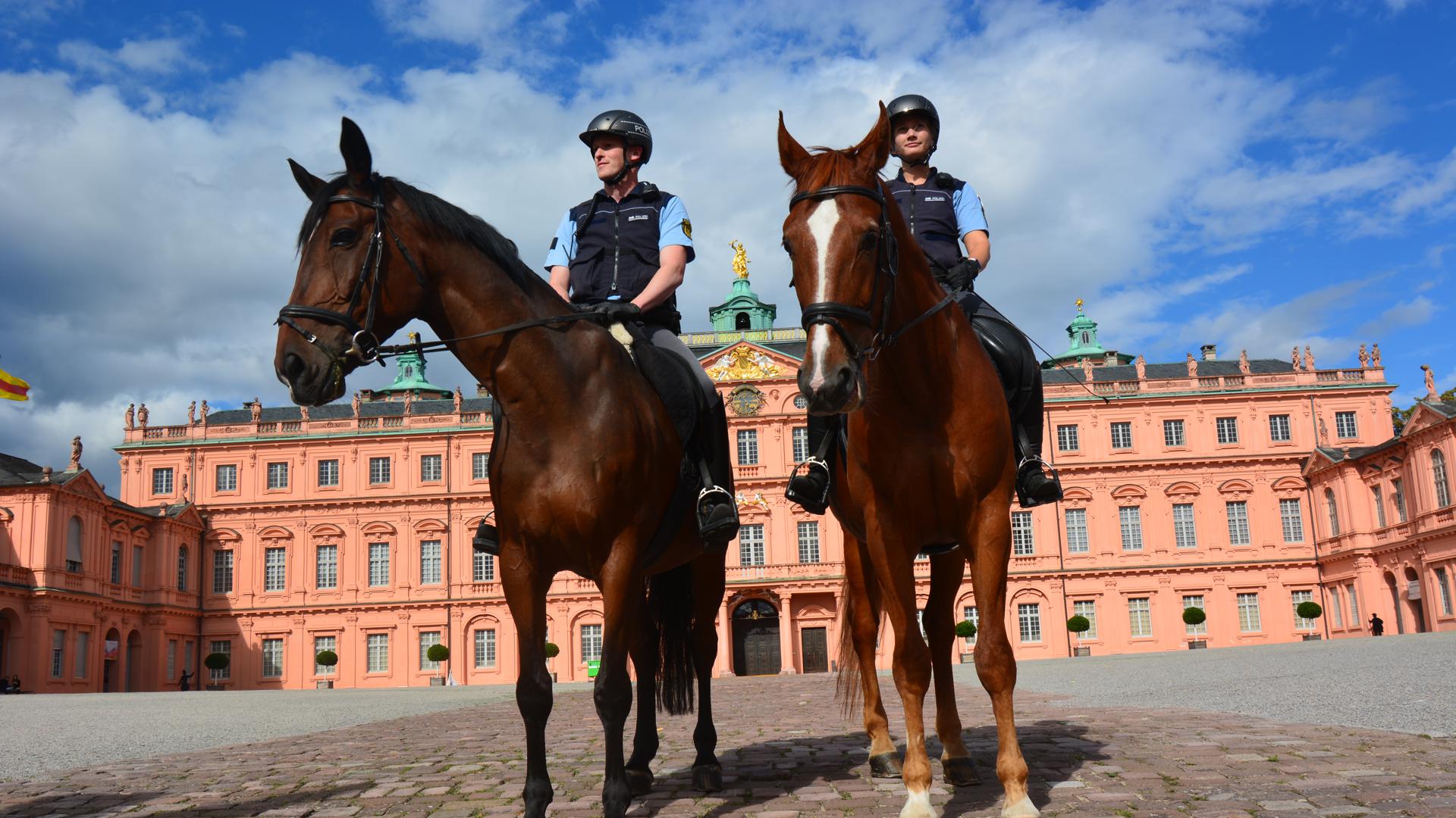 Zwei Polizisten auf Pferden vor einem Schloss. 