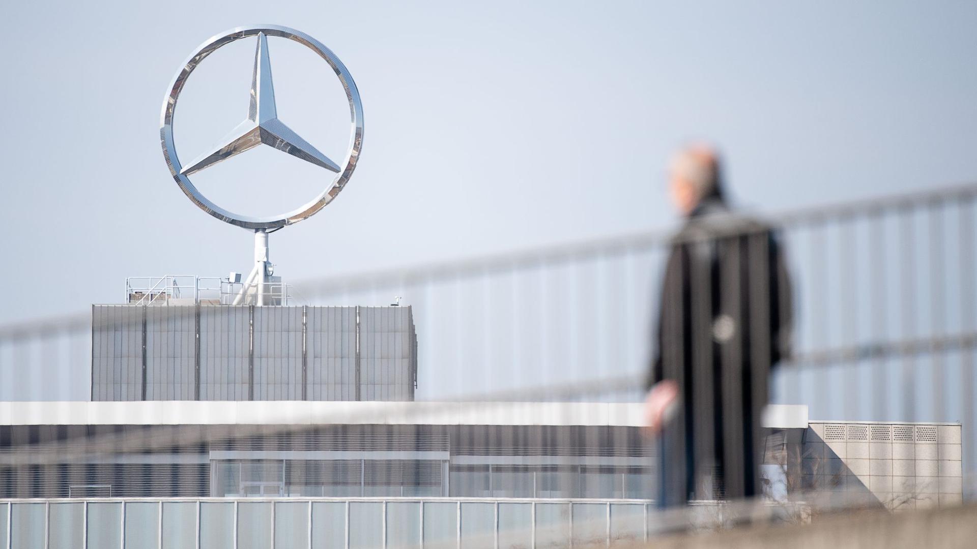 Ein Mitarbeiter von Daimler geht vor einem Mercedes-Stern Richtung Werk.