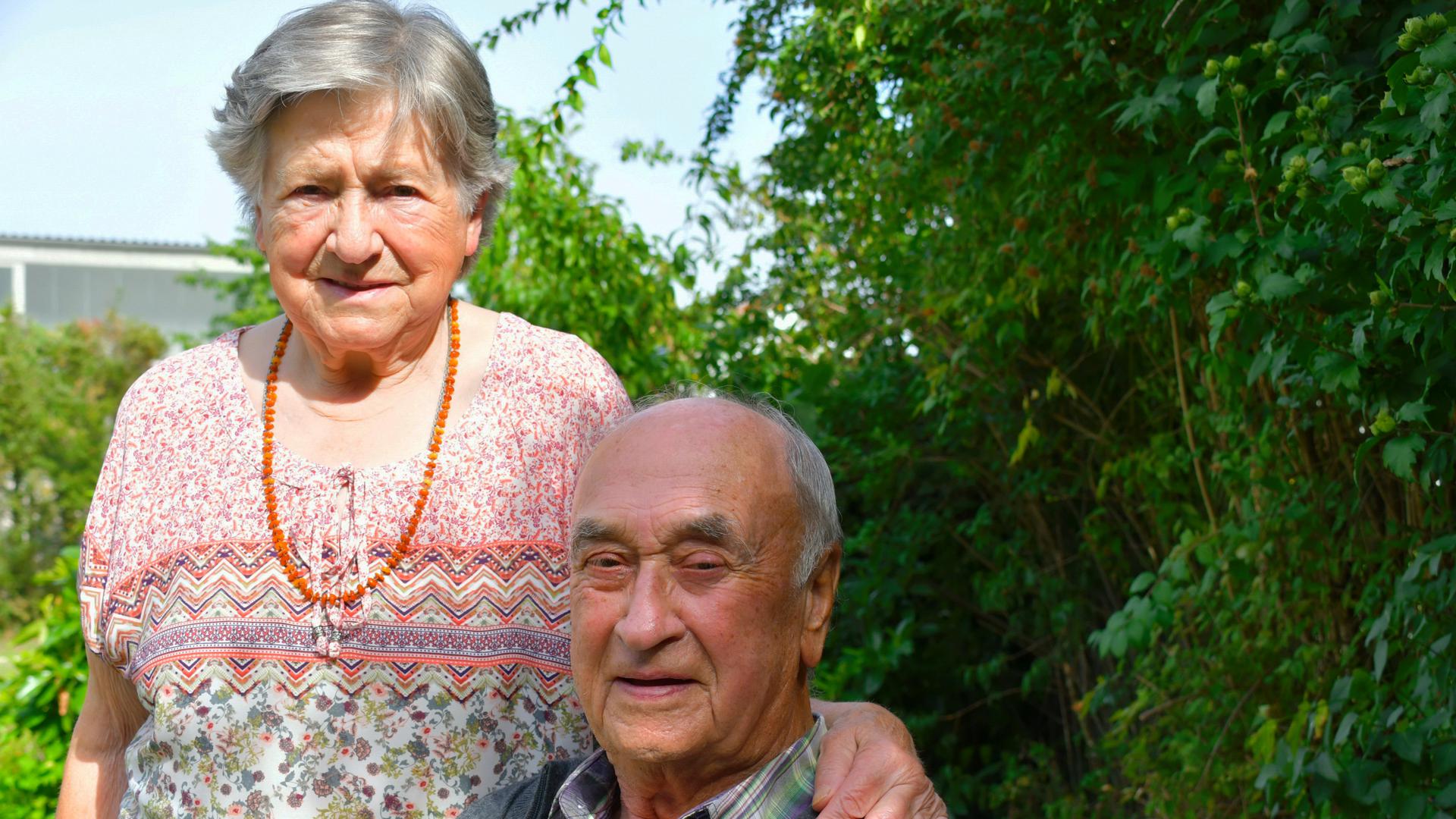 Älteres Ehepaar vor einem grünen Busch.