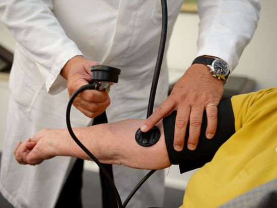 Ein Hausarzt misst in seiner Praxis einer Patientin den Blutdruck. 