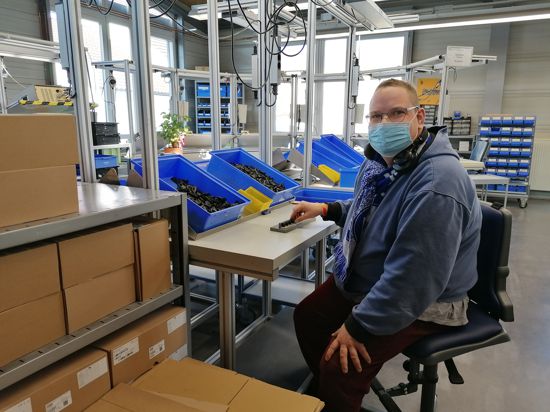 Matthias Rahner sitzt in einer Werkstatt an einem Tisch, auf dem mehrere, kleine, blaue Kisten stehen.