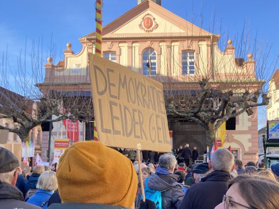 Bei einer Demonstration hält eine Frau ein Schild mit der Aufschrift „Demokratrie - leider geil“ in die Höhe. Vor ihr steht eine Menschenmenge vor dem Rastatter Rathaus. 