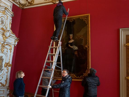 Eine Frau steht auf einer Leiter und hägt ein Gemälde auf.           