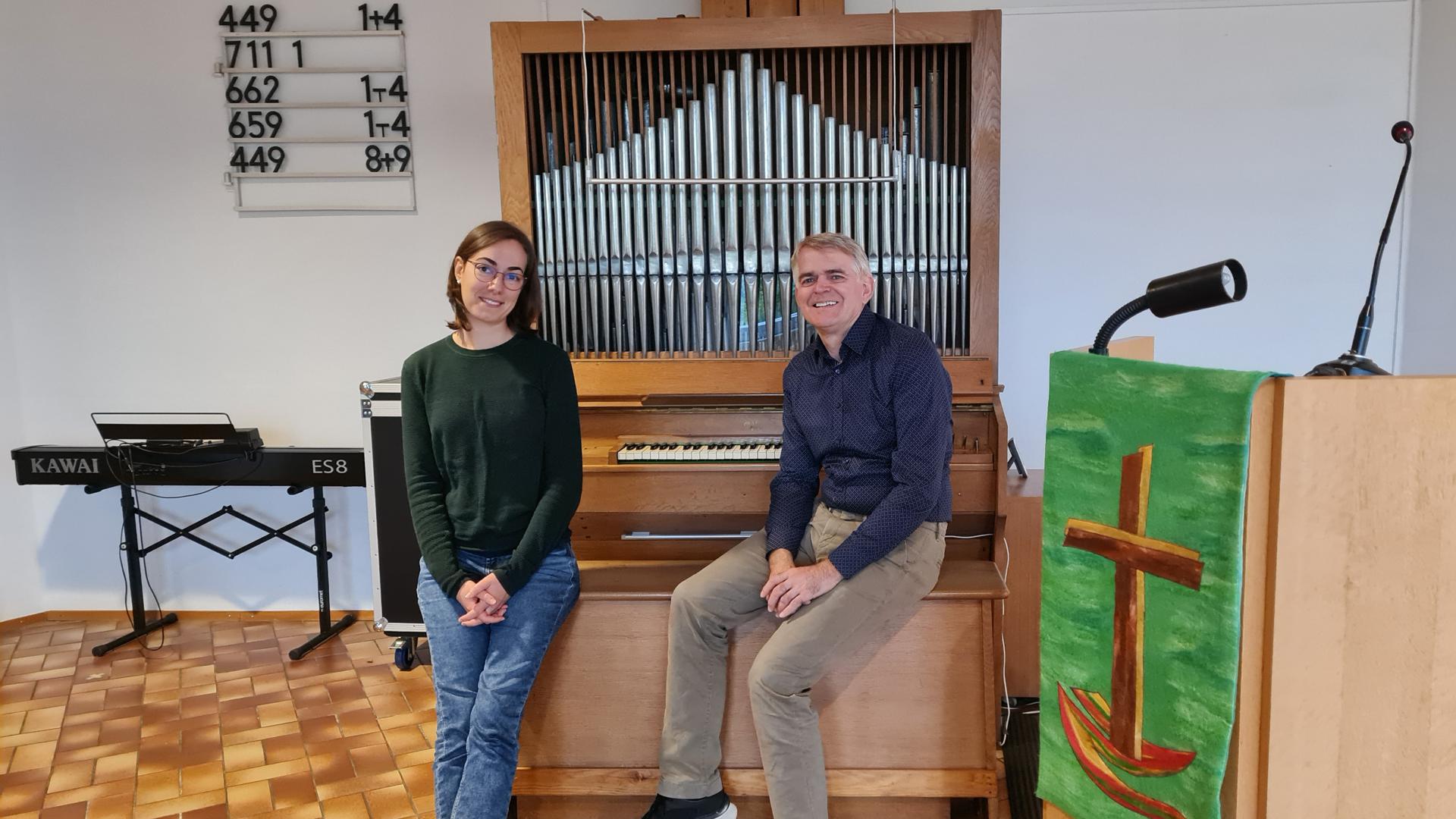 Eine Frau und ein Mann sitzen vor einer Orgel. 