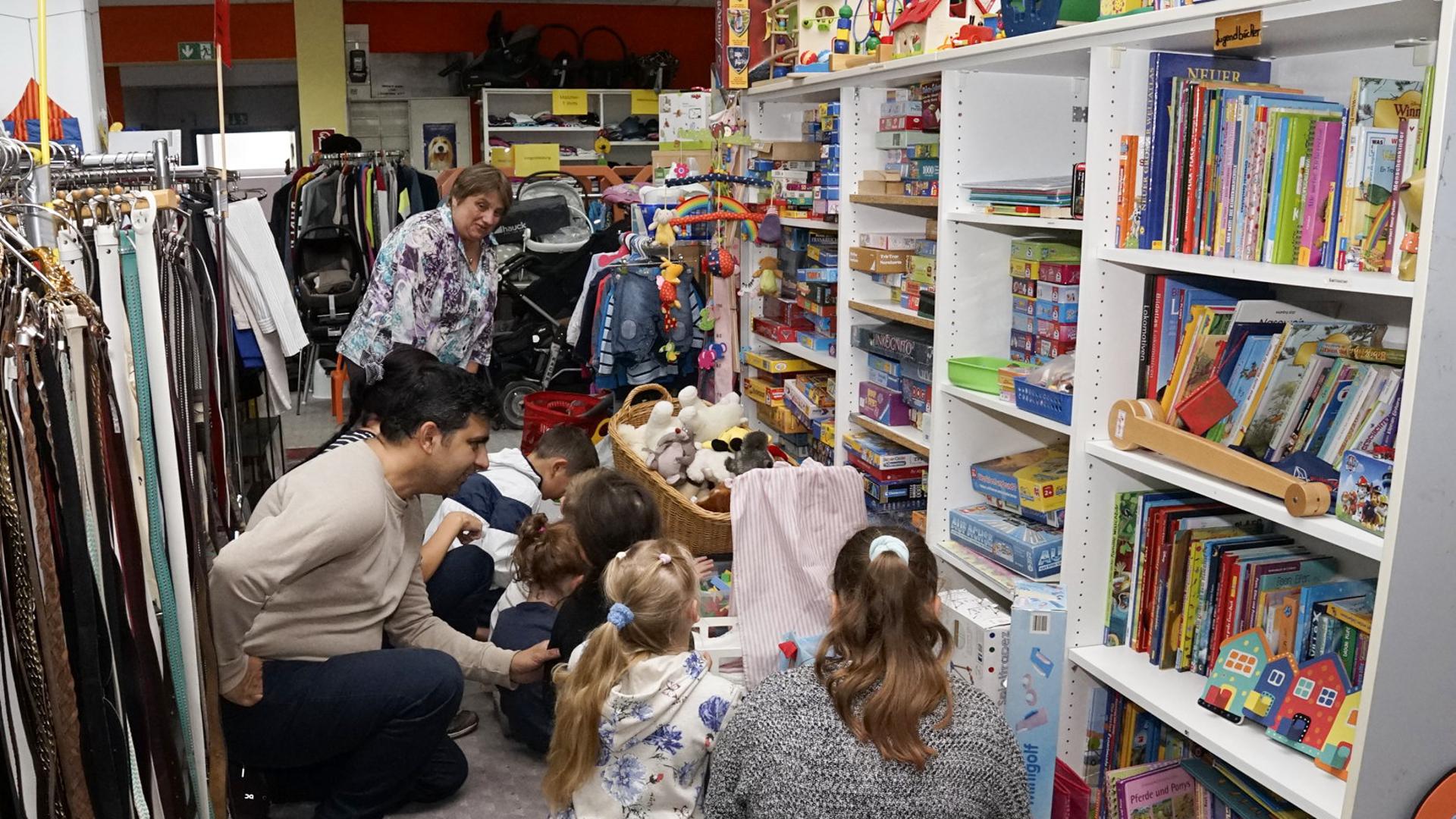 Gordana Stanicic von der Caritas in Rastatt betrachtet zusammen mit Kindern und Erwachsenen das Spielzeugangebot im Secondhandladen der Organisation.