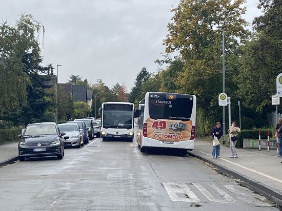 Blick in eine Straße, auf der links Autos parken und rechts ein Bus steht. Ein weiterer Bus kommt angefahren, der Platz ist eng.