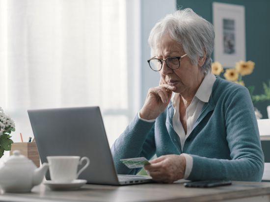 Ältere Dame sitzt mit ratlosem Gesichtsausdruck und einer Bankkarte in der Hand vor dem Computer.