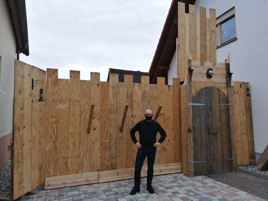 Marcel Lang steht vor einer aus Holzlatten gebauten Front, die eine Burg darstellt.