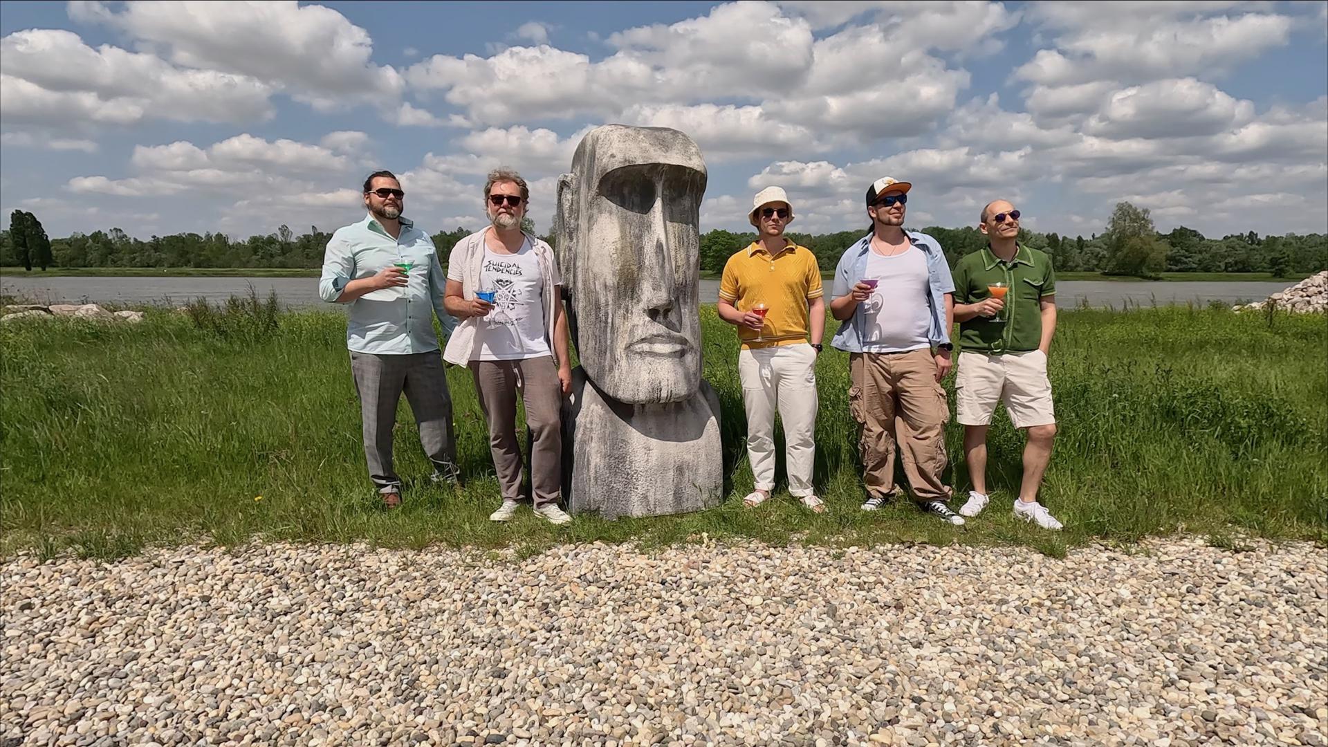 Für das Cover ihres Sommerhits „Der erste Sommer“ haben sich  fünf der Mitglieder der Band „Tacheles!“ auf dem Gelände des Kieswerks in Steinmauern um einen Moai aus Plastik gruppiert, Martinigläser mit bunten Flüssigkeiten in der Hand-.