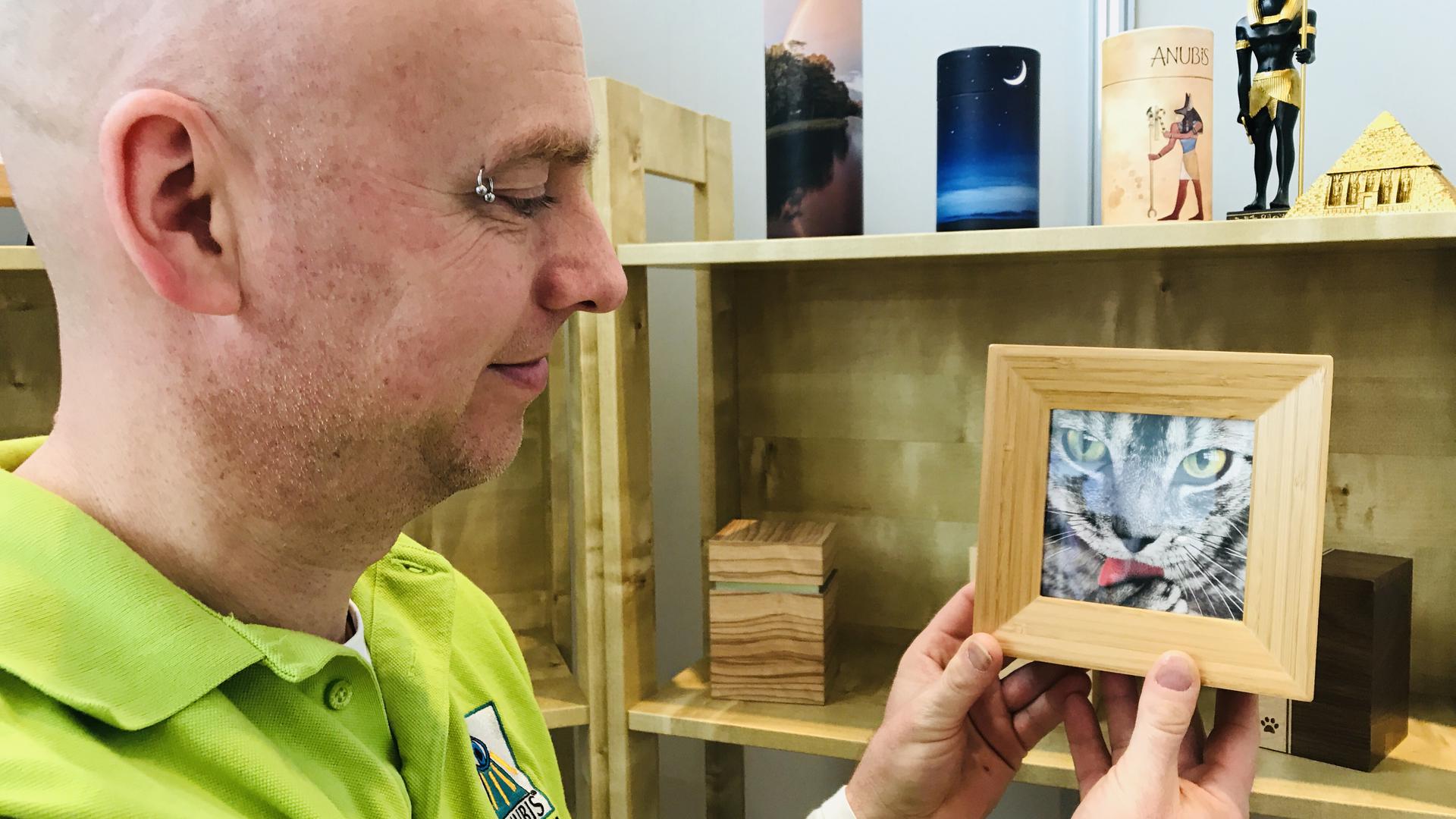 Christian Richers zeigt einen Holzbilderrahmen. Er ist aufklappbar. Im Innern könnte das Säckchen mit der Asche der verstorbenen Katze aufbewahrt werden.