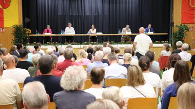 Blick in eine gut besuchte Halle, auf dem Podium die fünf OB-Kandidaten für Rastatt, im Zuschauerraum steht ein Fragesteller