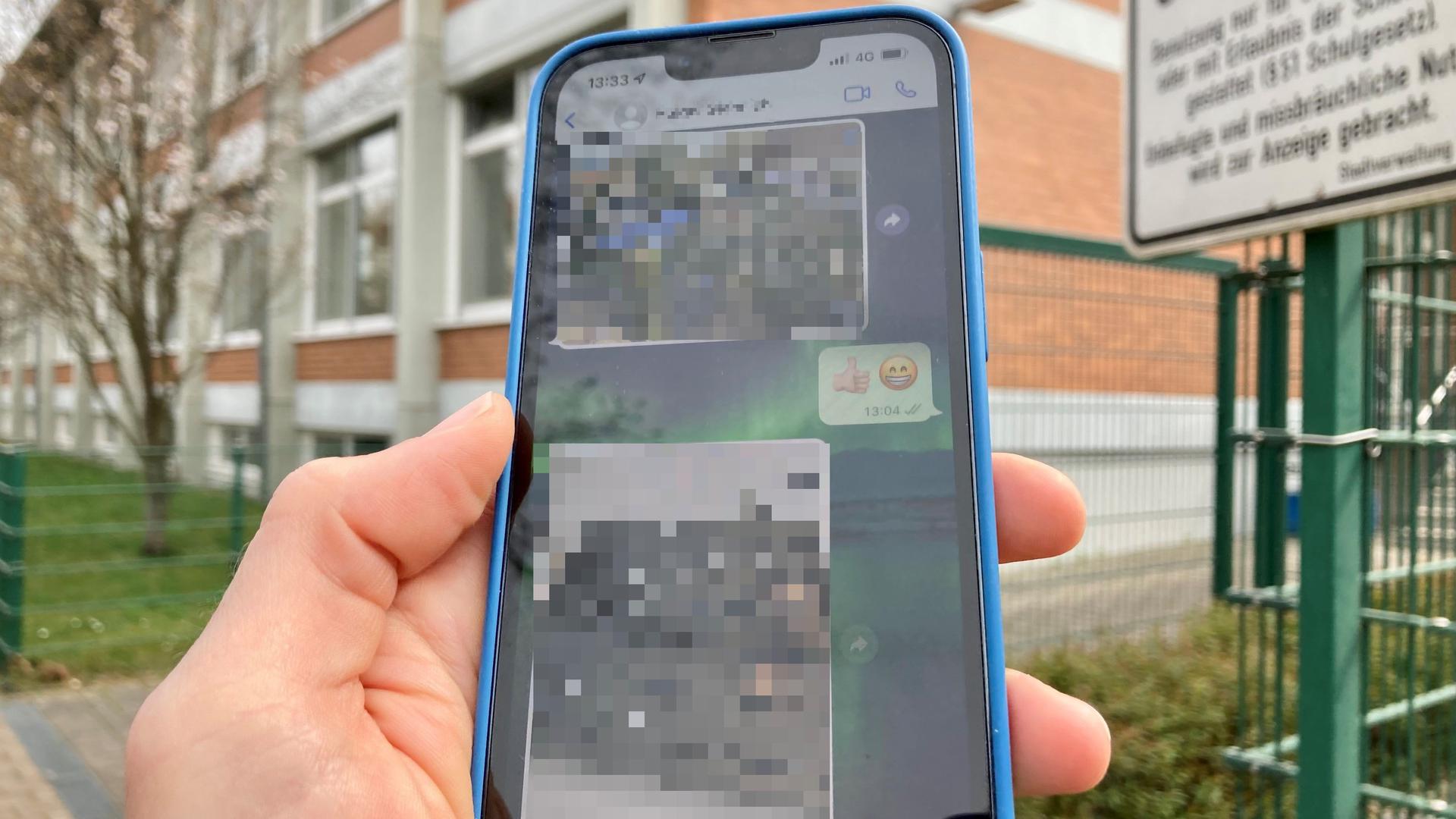 Ein Handy mit gepixelten Aufnahmen vor einer Schule.