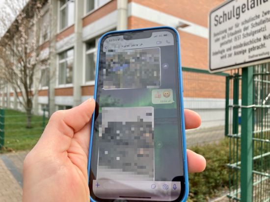 Ein Handy mit gepixelten Aufnahmen vor einer Schule.