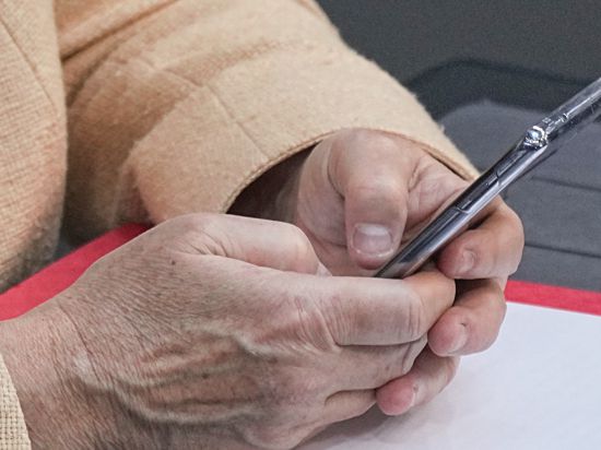 Detailaufnahme der Hand einer älteren Person, die ein Smartphone hält.