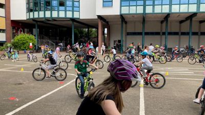 Ein Mädchen absolviert auf ihrem Fahrrad einen Geschicklichkeitsparcours. Im Hintergrund sind weitere Kinder auf Fahrrädern auf dem Schulhof der Muggensturmer Albert-Schweitzer-Schule zu sehen