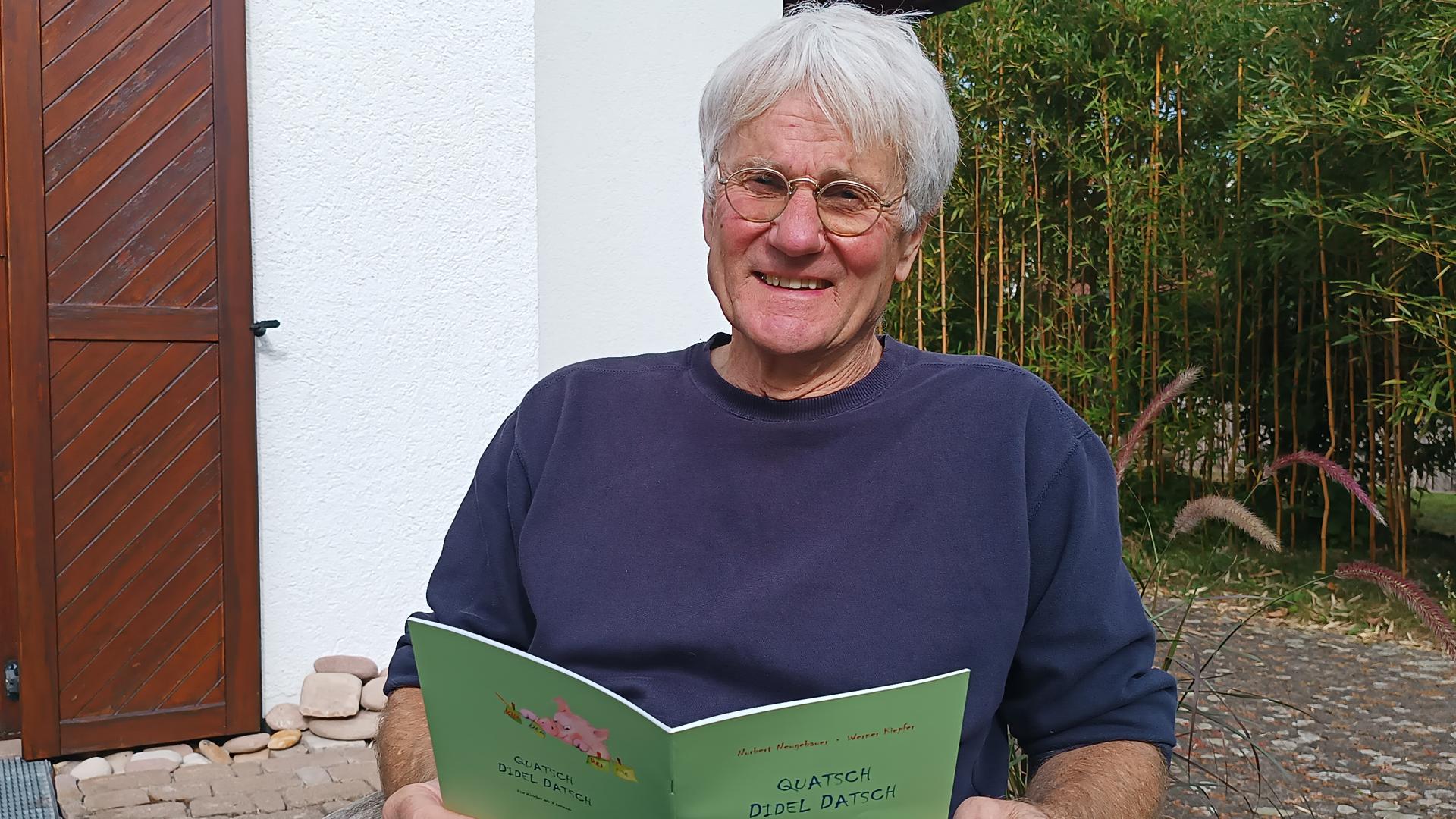 Norbert Neugebauer aus Rauental sitzt in seinem Garten und hält sein Buch „Quatschdideldatsch“ in Händen.
