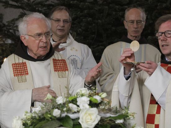 Zwei Pfarrer, Pater Anton (links) und Provinzialminister Dr. Cornelius Bohl (rechts), feiern das Abendmahl. Bohl hält eine Hostie in der Hand.