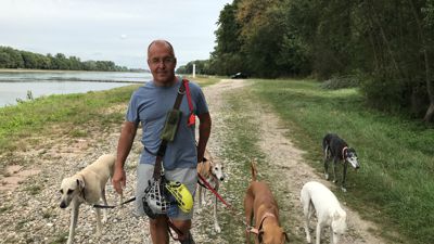 Ein Mann mit fünf Hunden an einem Flussufer.