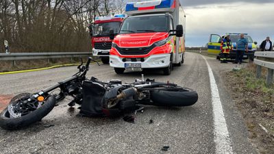 Unfallfoto: Ein beschädigtes Motorrad liegt auf der Straße, dahinter steht ein Rettungswagen.