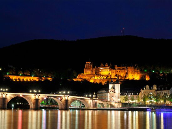 Die Lichter der Heidelberger Altstadt mit Schloss und Alter Brücke spiegeln sich im Neckar.
