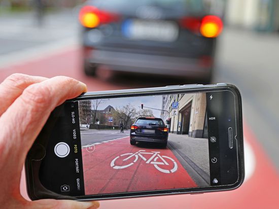 Auf einem Smartphone ist das Bild eines Autos zu sehen, das auf einem Radstreifen hält.