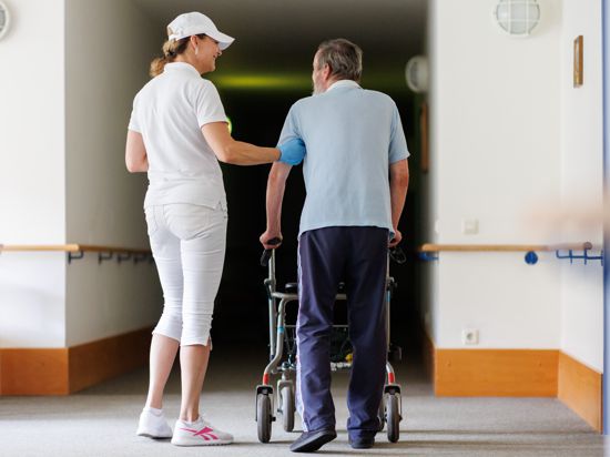Svetlana, ambulante Pflegefachkraft, begleitet einen Bewohner des Betreuten Wohnens mit seiner Gehhilfe durch das Gebäude. 