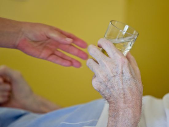 Eine Krankenpflegerin reicht einem Patienten in der Onkologie im Klinikum in Nürnberg ein Glas Wasser.