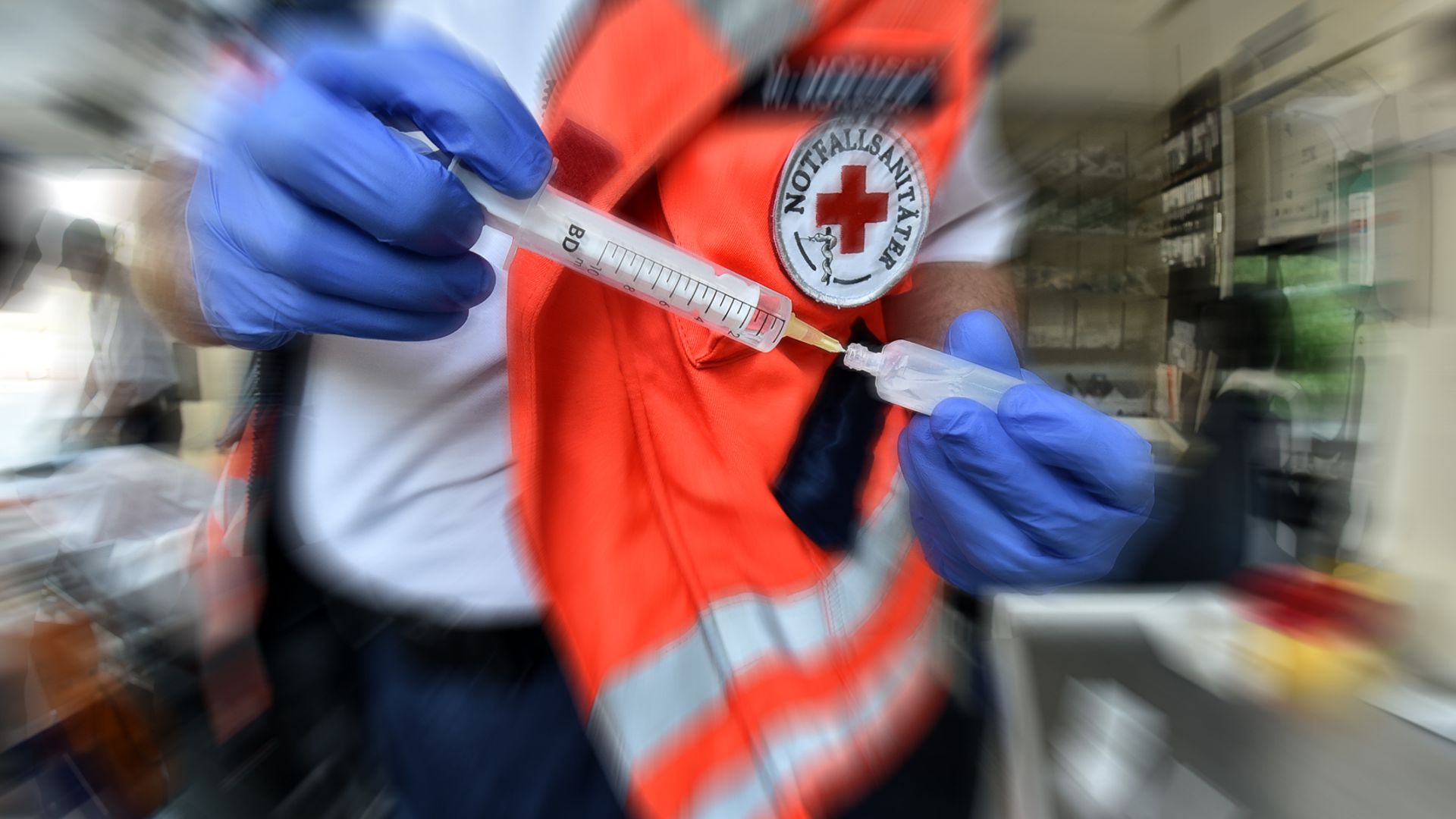 Mit blauen Handschuhen zieht ein Sanitäter die Spritze für einen Patienten auf (Symbolbild)