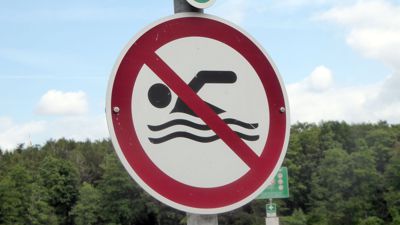 Ein Schild weist an einem Gewässer auf ein Badeverbot hin.