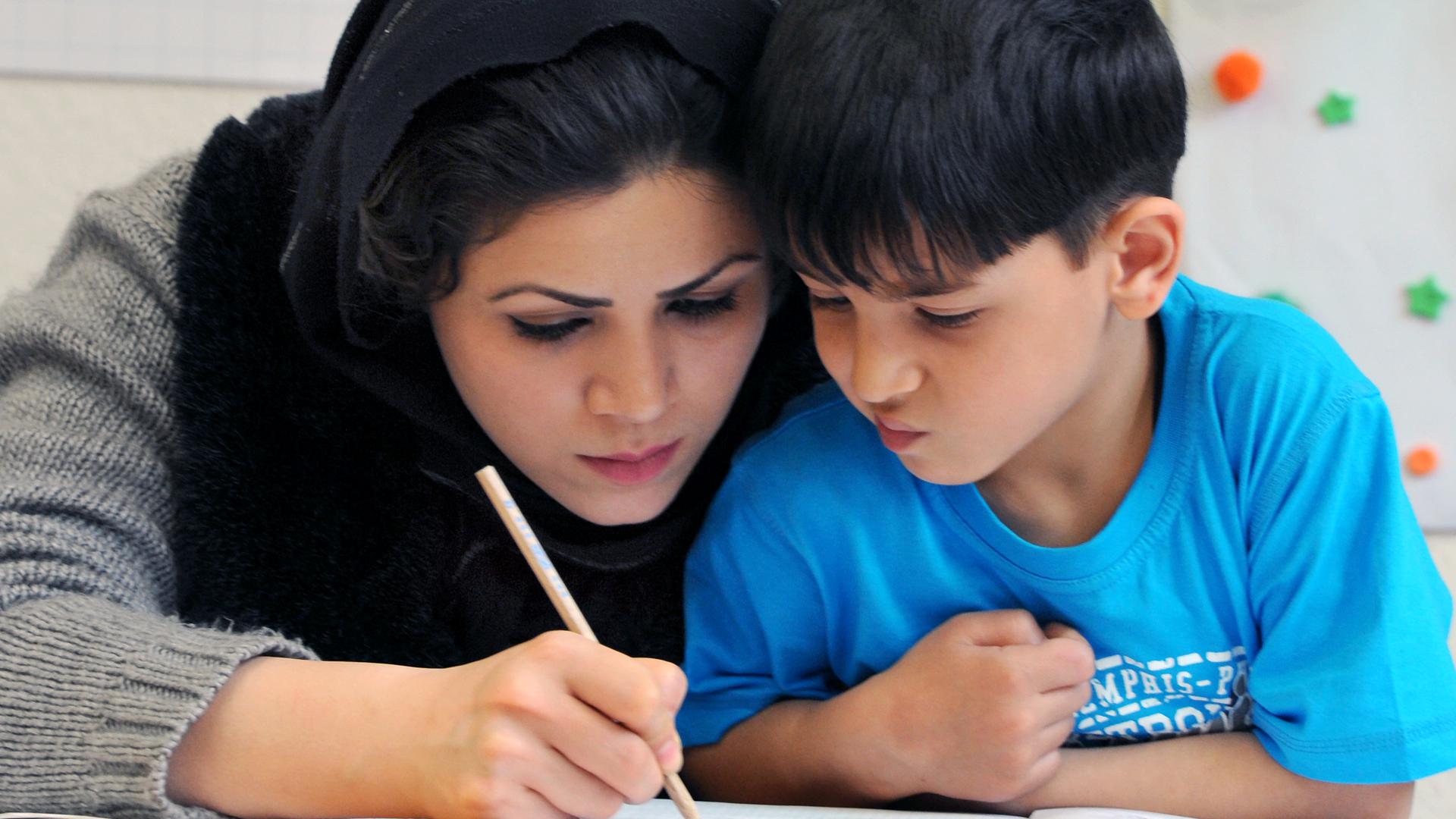 In einem Integrationskurs „Deutsch als Fremdsprache“ an der Volkshochschule Leipzig schreibt Kobra Soltani aus Afghanistan mit ihrem fünfjährigen Sohn Masoud.