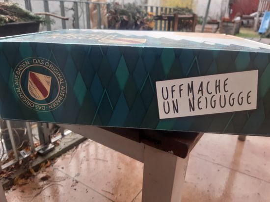 Kiste mit Dialekt-Aufschrift: Ufmache un Neigugge.