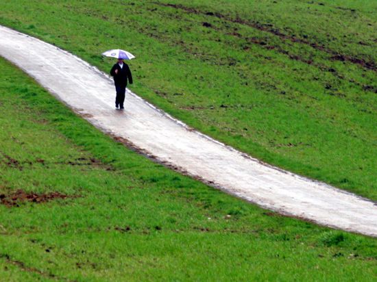 Ein Mann läuft am Sonntag (24.04.2005) bei Löffingen (Landkreis Breisgau-Hochschwarzwald) mit einem Regenschirm auf einem Feldweg durch grüne Felder. Bis zur Wochenmitte soll es nach Angaben der Meteorologen in Baden-Württemberg weiter wechselhaft mit Schauern bleiben. Foto: Patrick Seeger dpa/lsw +++(c) dpa - Bildfunk+++