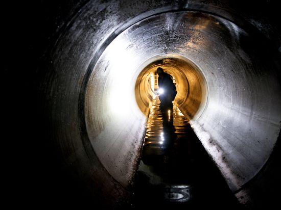 Ein Arbeiter schaut sich einen Teil eines Wasserkanales unter der Erde an.