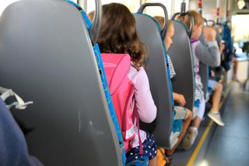 Kinder sitzen mit ihrem Ranzen in einem Schulbus.
