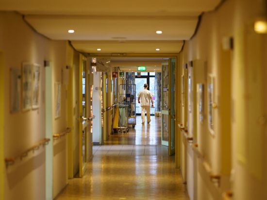 Ein Pfleger (hinten) geht einen der Gänge eines Alten- und Pflegeheims entlang.