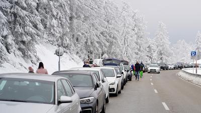 Autos parken an einer Straße vor einem verschneiten Wald im für Ausflügler beliebten Gebiet Mummelsee im Schwarzwald. 