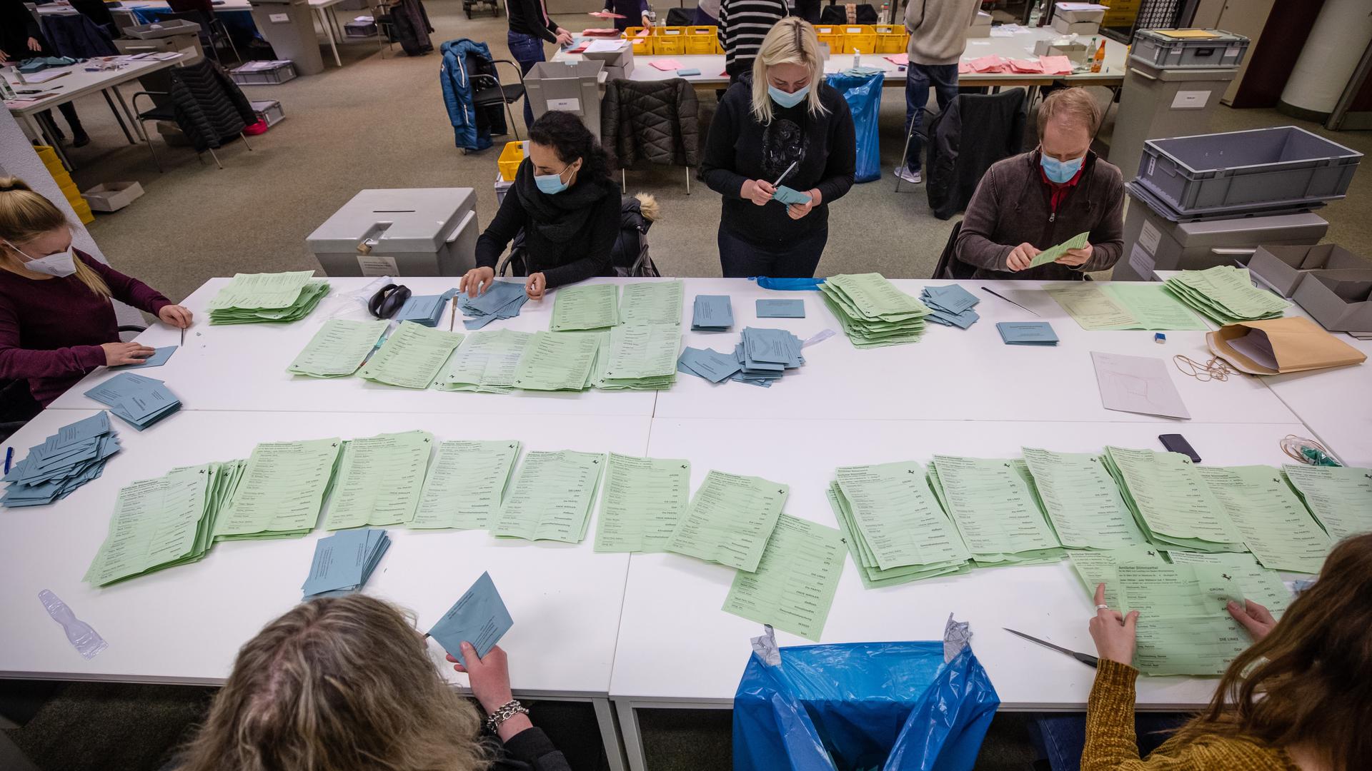 Wahlhelferinnen und Wahlhelfer zählen und kontrollieren in einer Außenstelle des Statistischen Amtes Stimmzettel aus.