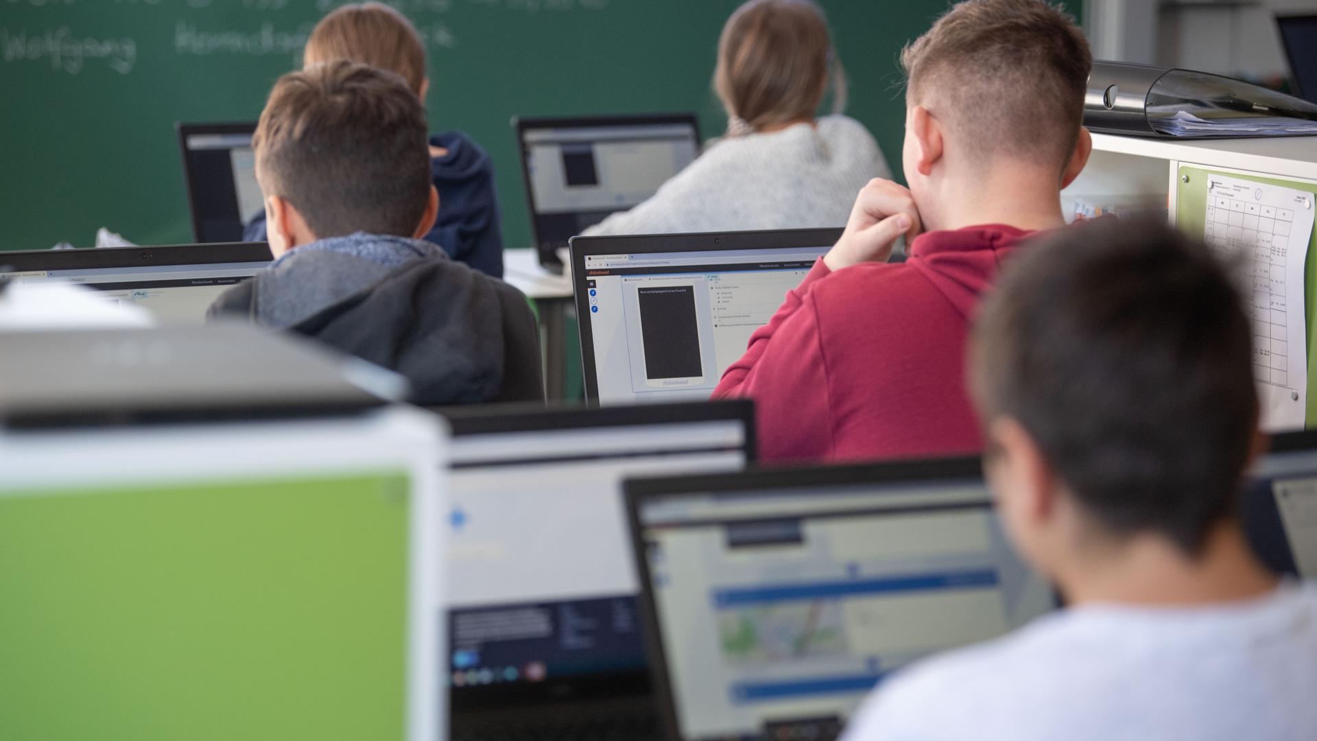 Schüler mit Laptops sitzen in einem Klassenzimmer.
