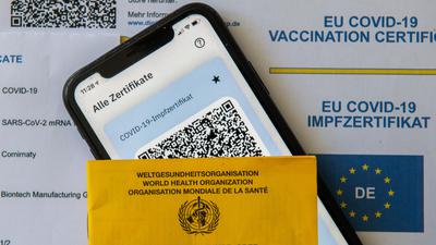 Ein Impfpass und ein Smartphone, auf dem die App CovPass läuft, liegen auf einem Impfzertifikat, das von einer Apotheke ausgestellt wurde. Der digitale Nachweis ist eine freiwillige Ergänzung des weiter gültigen gelben Impfheftes aus Papier. Deutschland setzt damit ein Vorhaben der Europäischen Union um. +++ dpa-Bildfunk +++