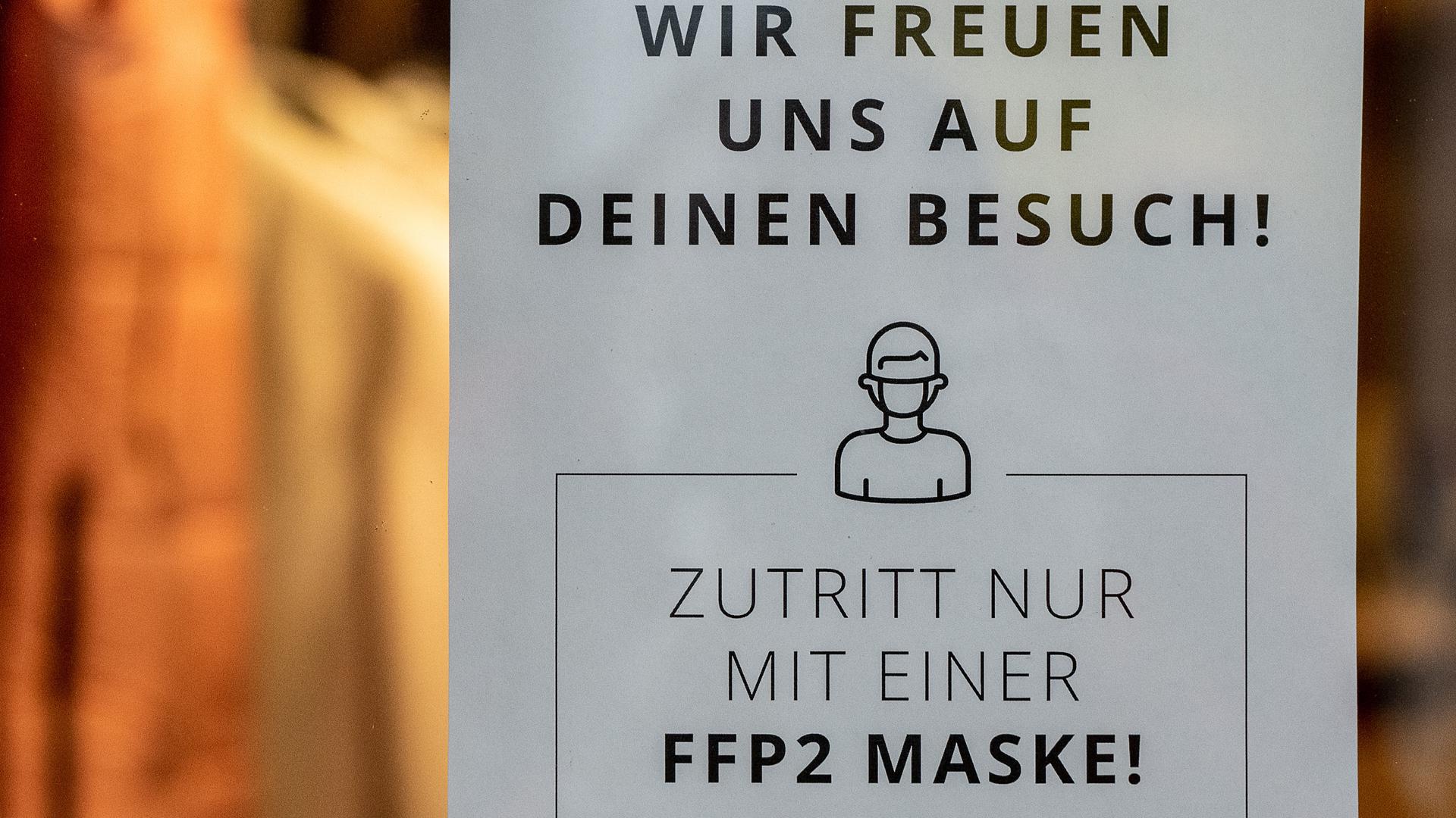 Ein Schild mit der Aufschrift "Zutritt nur mit einer FFP2 Maske!" ist an einem Eingang zu einem Bekleidungsgeschäft in der Innenstadt zu sehen.