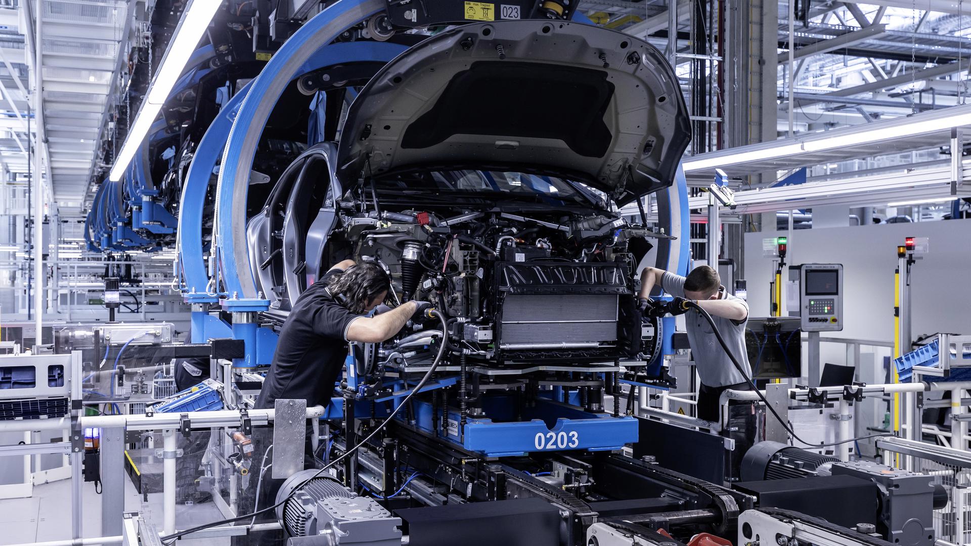 Zwei Arbeiter von Mercedes-Benz verbinden bei der Produktion des EQS die Karosserie mit dem Antrieb.