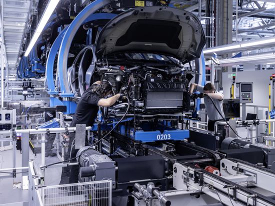 Zwei Arbeiter von Mercedes-Benz verbinden bei der Produktion des EQS die Karosserie mit dem Antrieb.